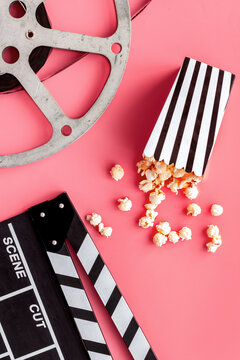 Movie premiere concept. Clapperboard, film stock, popcorn on pink background top view