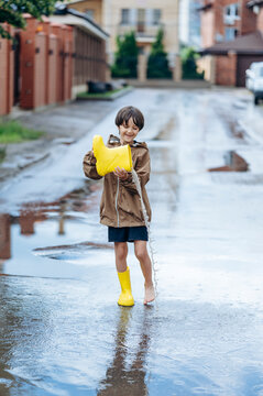 Smiling boy outdoors pours water from a yellow boot into a puddle