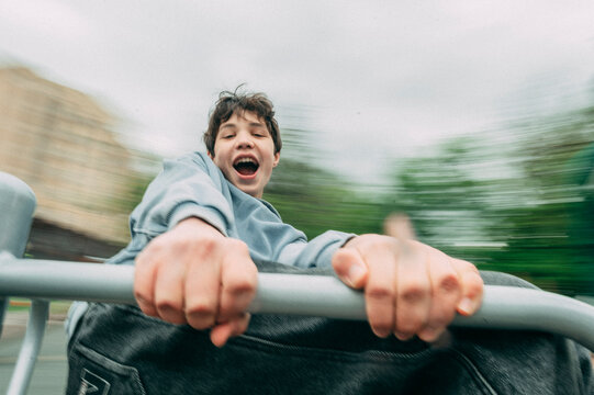 Laughing teenager rides a fast playground carousel