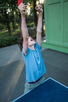 A teenage boy celebrates winning a table tennis match outdoors