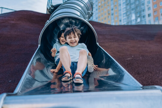 Two happy brothers ride a metal slide at the outdoor playground