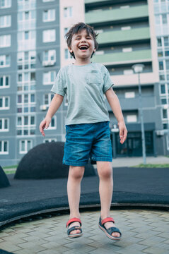A happy boy jumps on a trampoline at an outdoor city playground