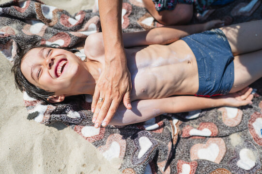 Mother applies sunscreen to laughing boy on the beach