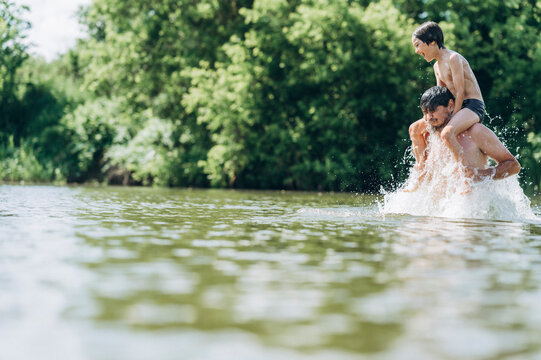 Father carrying his son piggyback in a river splashing water