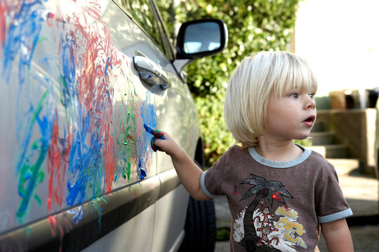 Child finger painting on a car outdoors causing a disaster
