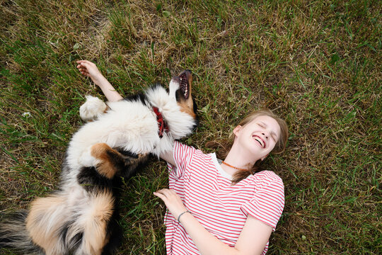 A laughing girl pets her playful dog on the summer grass