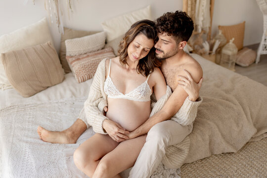 A man embraces a pregnant woman on a bed indoors