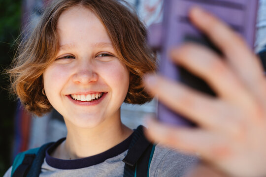 A smiling teenage girl takes a selfie with her smartphone outdoors