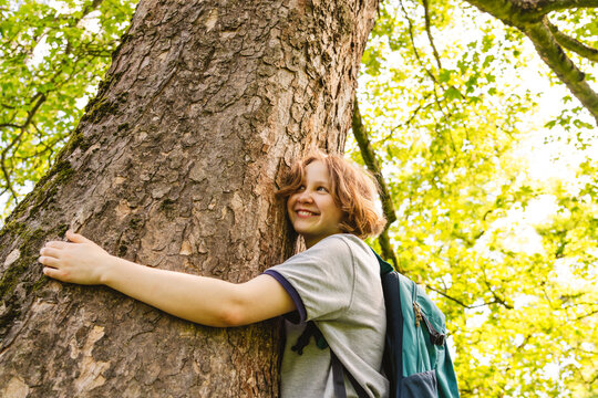 A smiling girl hugs a large tree trunk in the forest