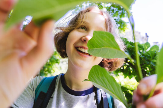 Smiling teenage girl exploring nature looking through green leaves