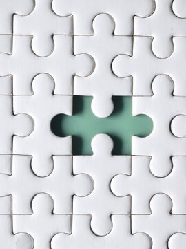 Vertical close-up view of a clean white jigsaw puzzle matrix with one empty central slot showing a green background, symbolizing a missing link, critical position, or core problem.