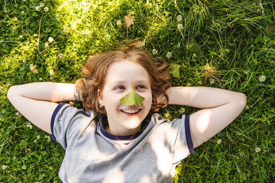 A smiling girl enjoys the grass with a gingko leaf on her nose
