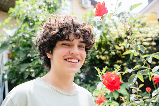 A young man with curly hair smiles in a summer garden