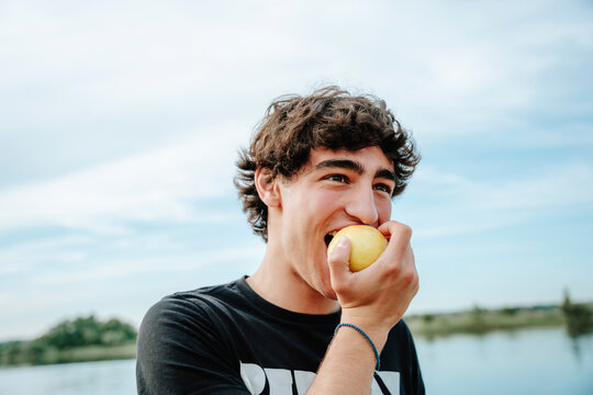 Smiling man eats a fresh apple outdoors against the sky