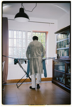 A man hangs laundry on a drying rack indoors during the morning
