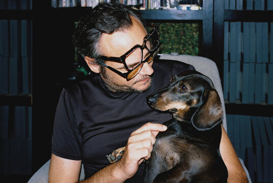 Male pet owner affectionately holds his dachshund dog indoors