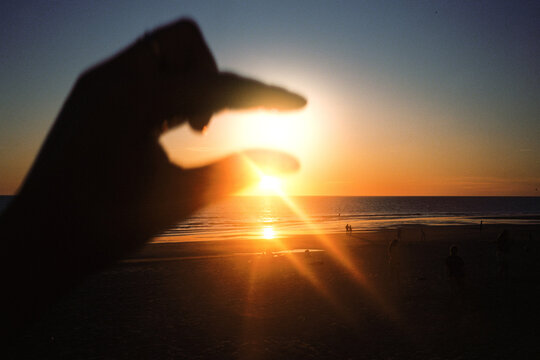 Mature woman holds the setting sun between her fingers on the beach