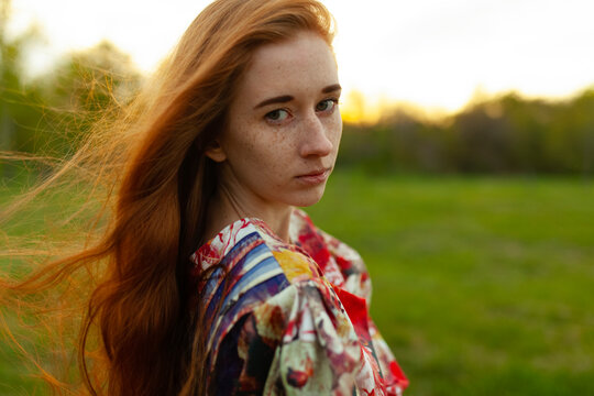 Female with red hair and dress in a park at sunset