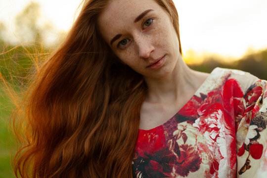 Female with freckles wears a voluminous dress in a park at sunset