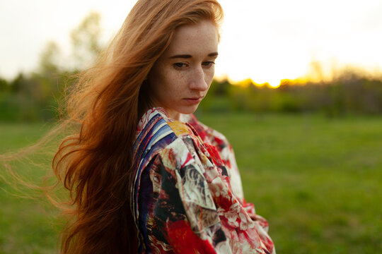 Pensive woman with long red hair in a park at sunset