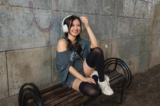 Happy woman sits on a city bench listening to music in the evening