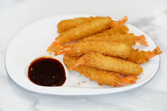 High angle view of golden deep fried ebi tempura prawns served on a white oval platter. Japanese breaded shrimp appetizer with dark dipping sauce in a built-in bowl.