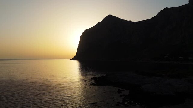 Breathtaking sunrise drone silhouette of Capo Gallo headland in Palermo, Sicily. The Mediterranean reserve awakens under golden morning skies Italian summer holiday