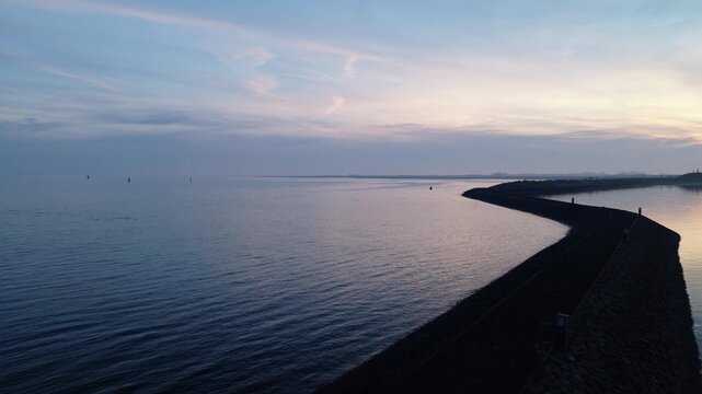 Drone pulls away from a navigation beacon in the Wadden Sea near Terschelling, Friesland, Netherlands, revealing stone breakwaters, calm tidal water and tranquil blue-hour coastal scenery.