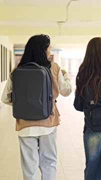 Two students with backpacks walk through a bright campus corridor as one points ahead, suggesting directions or orientation.