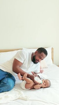 Father gently bottle-feeding his baby on a cozy bed in a bright, minimalist bedroom, capturing tender bonding and everyday family life.