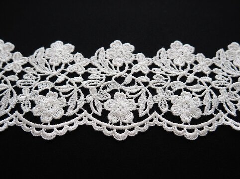 Delicate white floral lace ribbon with scalloped edges isolated on a contrasting black surface background for crafting.
