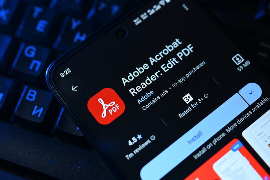 VEHARI, PAKISTAN - JULY, 30, 2026: Adobe Acrobat Reader app download page on smartphone screen next to a backlit computer keyboard