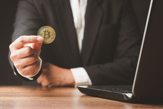 Person Holding Cryptocurrency Coin Beside Laptop
