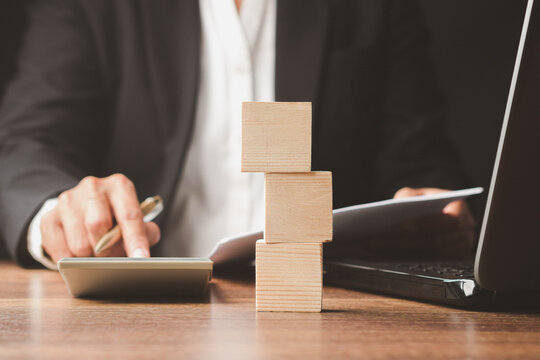 Person Calculating Finances with Stacked Wooden Blocks