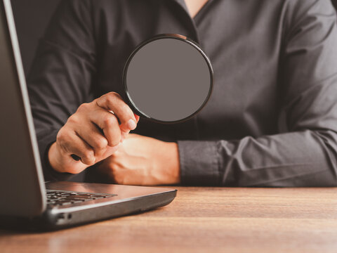 Person Holding Magnifying Glass Beside Laptop