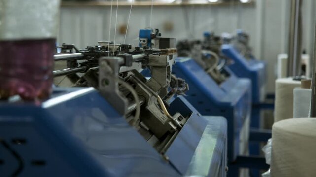 Multiple automated knitting machines operate continuously inside modern textile factory. Precision equipment supports efficient industrial manufacturing with synchronized production lines.