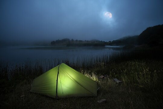 tent camping on Biviere lake in a foggy night landscape with a full moon, Nebrodi Park, Sicily, Italy 