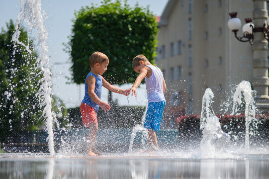 Happy Brothers Playing in Splash Fountain on Sunny Summer Day in City Park