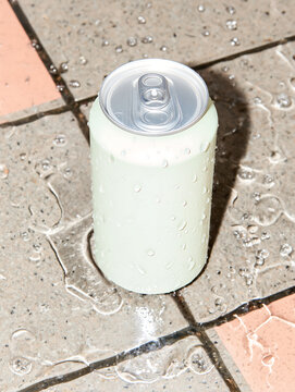 Top view of tin soda can standing on multicolored tiled floor covered in water. Metal soda packaging for showcasing food products.