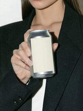 Long-haired young woman in dark business suit holding chilled soda can against wall background. Lemonade beverage in a sealed aluminum container.