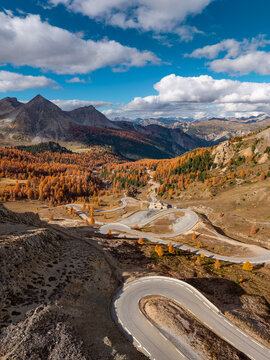 Aerial view of the scenic winding D902 mountain road at Col d&rsquo;Izoard in the French Alps, Hautes Alpes, with Napoleon Refuge and scenic autumn larch forest in the Briancon region