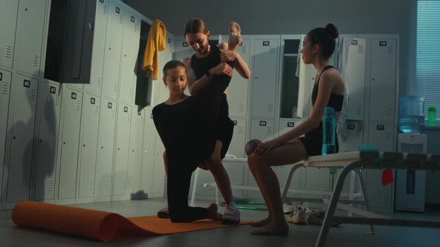 Teenage Gymnast Holding Perfect Vertical Leg Stretch on Training Mat. Teammates Allowing to Safely Push Boundaries of Flexibility. Physical Effort Required in Elite Rhythmic Gymnastics Schools.
