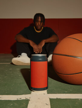 Aluminum soda can with bright red label on basketball court with young man in sportswear sitting near wall on background. Aluminum beverage packaging as an object of the food industry.