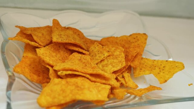 Human hand taking crispy tortilla nacho chips from a glass bowl