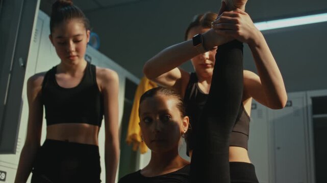 Gymnastics Studio Locker Room Where Young Schoolgirls Practicing Challenging Contortion Leg Extension. Serious Athletic Attitude and Deep Friendship Bonds During Demanding Pre Competition Rehearsal.