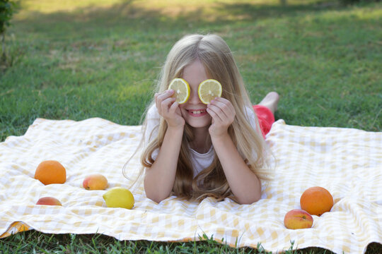 Happy little girl playing with fresh lemon slices during a summer picnic