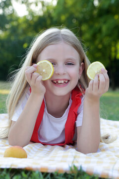 Happy little girl playing with fresh lemon slices during a summer picnic