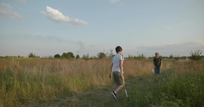 Two boys play badminton on nature. Teenagers spending time together. 4K 10-bit