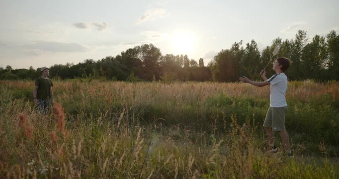 Two boys play badminton on nature. Teenagers spending time together. 4K 10-bit