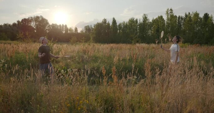Two boys play badminton on nature. Teenagers spending time together. 4K 10-bit